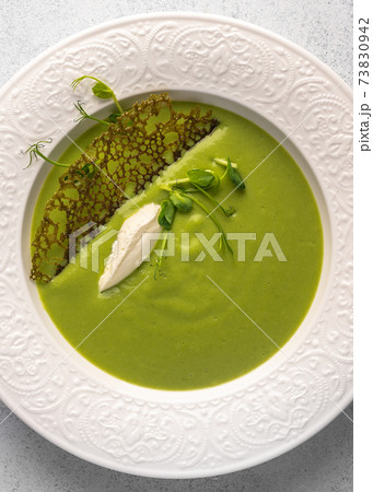 Vertical view soup puree of green peas and coconut milk with tuil and cheese quenelle 73830942