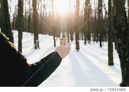 The guy holds a paper cup of coffee in his hand in the snowy forest 73831066