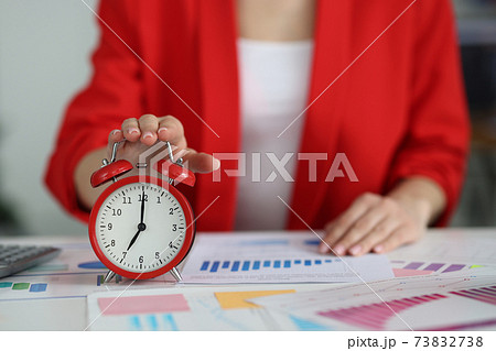 Woman in red jacket turning off alarm clock at table 73832738