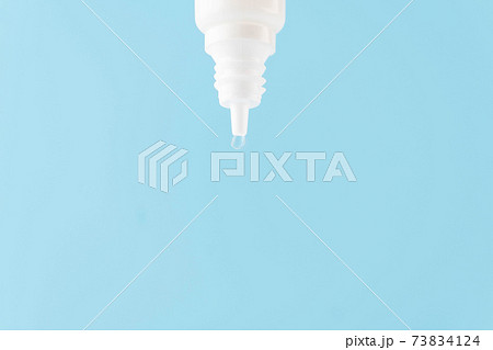 Eye drop or ear drop bottle with droplet on blue background. Pharmaceutical product. Copy space. Eye drop or ear drop bottle with droplet on blue background. Pharmaceutical product. Copy space. 73834124