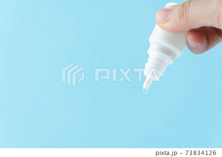 Female hand holding eye drop or ear drop bottle with droplet on blue background. Pharmaceutical product. Copy space. Female hand holding eye drop or ear drop bottle with droplet on blue background. Pharmaceutical product. Copy space. 73834126