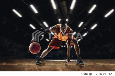 African-american young basketball player in action and flashlights over gym background. Concept of sport, movement, energy and dynamic, healthy lifestyle. African-american young basketball player in action and flashlights over gym background. Concept of sport, movement, energy and dynamic, healthy lifestyle. 73834142