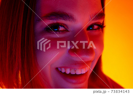 Caucasian woman's portrait isolated on orange studio background in multicolored neon light Caucasian woman's portrait isolated on orange studio background in multicolored neon light 73834143