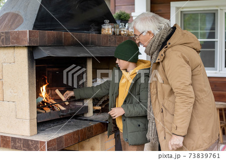 Cute youngster or teenager in warm jacket and beanie standing by fireplace Cute youngster or teenager in warm jacket and beanie standing by fireplace 73839761