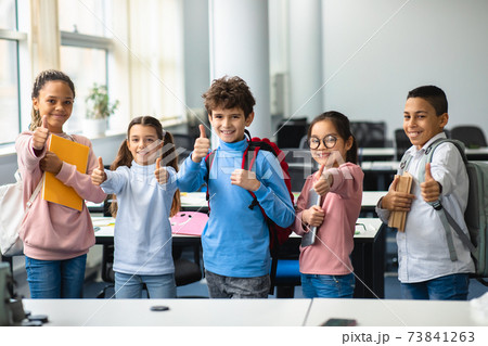 Smiling international schoolchildren showing thumbs up gesture 73841263