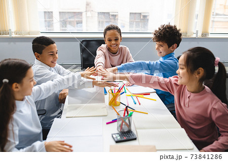 Diverse small schoolchildren putting hands together at classroom Diverse small schoolchildren putting hands together at classroom 73841286