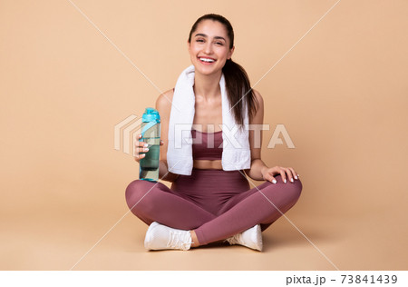 Sporty woman sitting on floor holding water bottle Sporty woman sitting on floor holding water bottle 73841439
