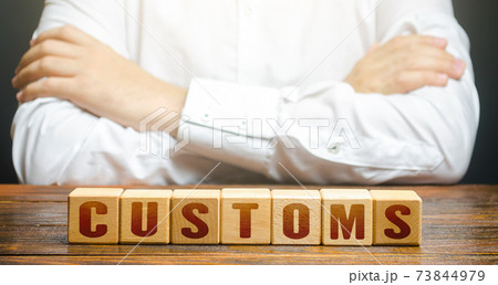 Man with folded hands on his torso and blocks with word Customs. Customs border control. Tariffs and taxes on the import of goods and products. Imports monitoring. Duties. Transportation and transit. Man with folded hands on his torso and blocks with word Customs. Customs border control. Tariffs and taxes on the import of goods and products. Imports monitoring. Duties. Transportation and transit. 73844979