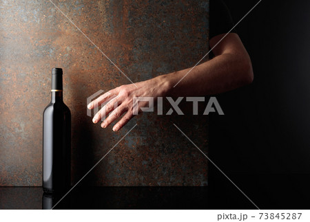 Hand reaches for a bottle of red wine. 73845287