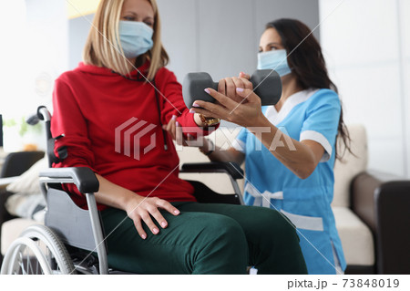 Doctor helps woman in wheelchair to do exercises with dumbbells Doctor helps woman in wheelchair to do exercises with dumbbells 73848019