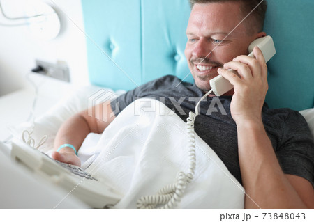 Smiling man lies in bed and talks on phone 73848043