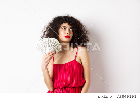 Elegant beautiful woman in red dress, waving with dollars and looking fabulous, standing on white background Elegant beautiful woman in red dress, waving with dollars and looking fabulous, standing on white background 73849191