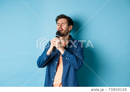 Romantic guy singing in microphone, performing on stage, standing on blue background Romantic guy singing in microphone, performing on stage, standing on blue background 73850130