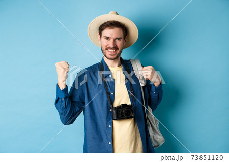 Happy tourist enjoying summer vacation, smiling and saying yes with fist pump, celebrating on holidays, feeling joy as finaly travel abroad, standing on blue background Happy tourist enjoying summer vacation, smiling and saying yes with fist pump, celebrating on holidays, feeling joy as finaly travel abroad, standing on blue background 73851120