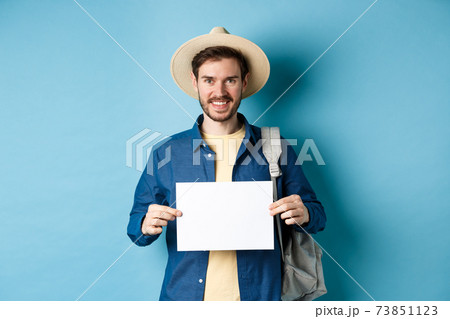 Happy tourist with backpack showing empty piece of paper, smiling at camera, standing on blue background. Concept of summer holiday and vacation Happy tourist with backpack showing empty piece of paper, smiling at camera, standing on blue background. Concept of summer holiday and vacation 73851123