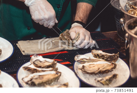 Chef in white gloves shucking a fresh oyster with knife. Chef in white gloves shucking a fresh oyster with knife. 73851491