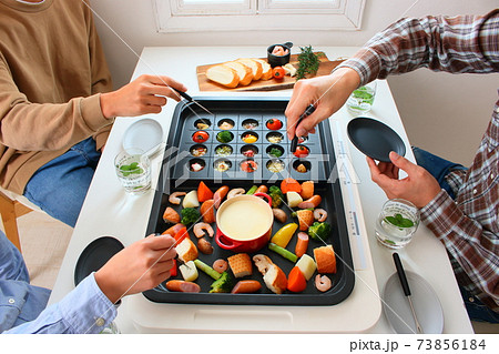 ホットプレートでアヒージョとチーズフォンデュをする家族の食卓風景 73856184