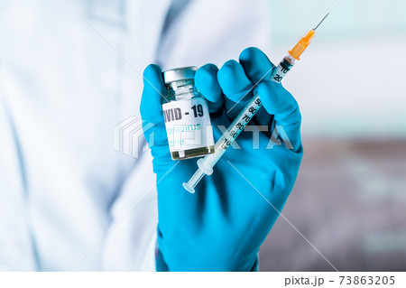 Woman doctor or nurse in uniform and gloves wearing face mask protective in lab holding medicine vial vaccine bottle with COVID-19 Coronovirus vaccine label 73863205