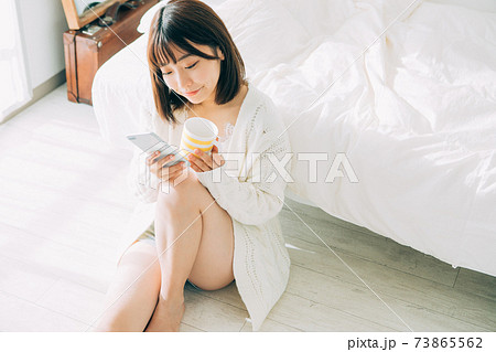 部屋でコーヒーを飲みながらスマホを見る女性 73865562
