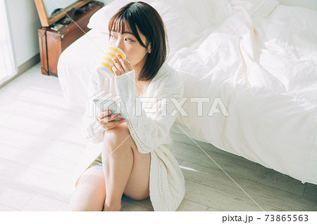 部屋でコーヒーを飲みながらスマホを見る女性 73865563