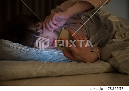 夜に布団の中で部屋スマホを見る女性 73865574