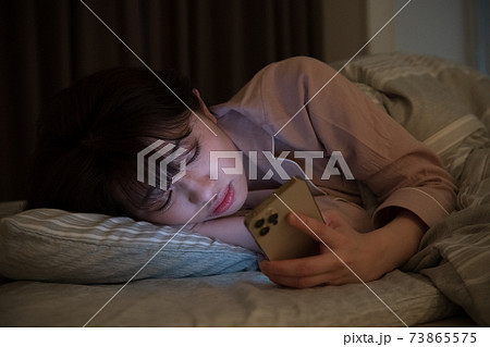 夜に布団の中で部屋スマホを見る女性 73865575