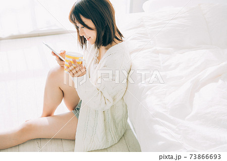 部屋でコーヒーを飲みながらスマホを見る女性 部屋でコーヒーを飲みながらスマホを見る女性 73866693