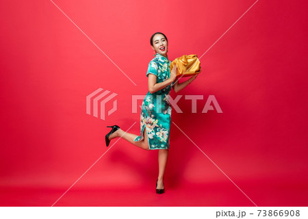 Happy smiling Asian woman in traditional costume holding gold gift box in red 73866908