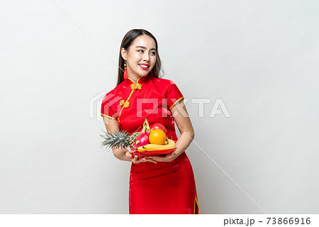 Young Asian woman in traditinal red cheongsam dress holding lucky fruits 73866916