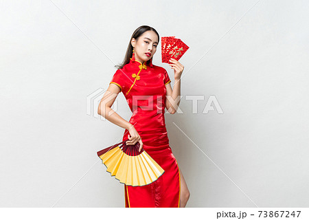 Asian woman in oriental cheongsam holding red envelopes or Ang Pao and fan 73867247