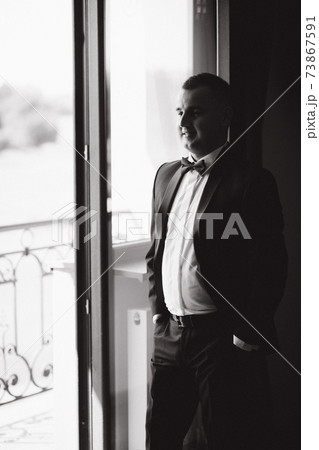 Groom stand in window by balcony at hotel. Handsome groom waiting for bride 73867591