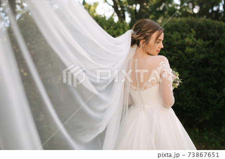 Elegand bride in white wedding dress hold bouquet of flowers. Big viel. Background of green bush Elegand bride in white wedding dress hold bouquet of flowers. Big viel. Background of green bush 73867651