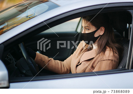 Beautiful young girl in a mask sitting in a car and put on protective gloves. Protective mask against covid-19, driver on a city street during a coronavirus outbreak Beautiful young girl in a mask sitting in a car and put on protective gloves. Protective mask against covid-19, driver on a city street during a coronavirus outbreak 73868089