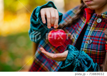A girl holding a red apple in her hands in the autumn garden on a blurred background, place for text. A girl holding a red apple in her hands in the autumn garden on a blurred background, place for text. 73869032