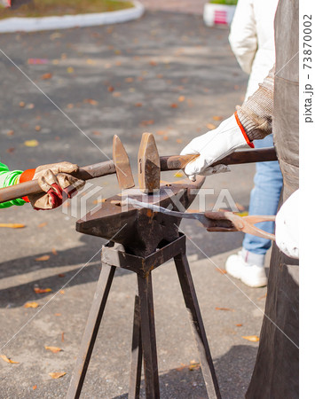 A blacksmith forges a metal blank on the anvil at a fair in the presence of spectators. A blacksmith forges a metal blank on the anvil at a fair in the presence of spectators. 73870002