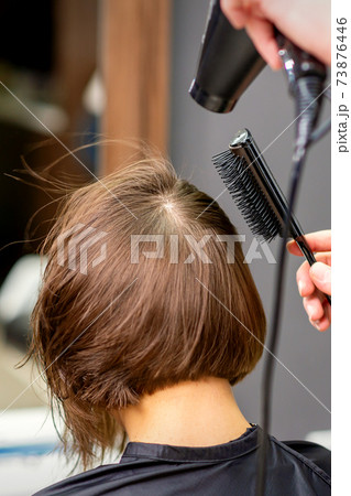 Hairdresser dries brown hair of woman 73876446