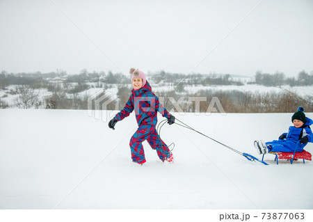 Happy boy and girl sledding from a hill in winter. Winter games outdoors. Happy boy and girl sledding from a hill in winter. Winter games outdoors. 73877063