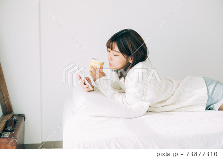 ベッドに寝転がってスマホを見る女性の写真素材