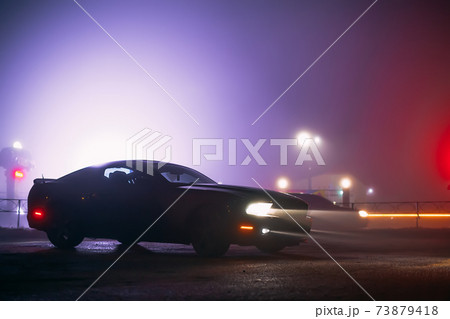Sport car in the shadows with glowing lights in low light at foggy night, or silhouette of sport car dark background. Selective focus 73879418