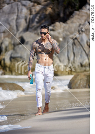 Athletic tattooed guy walking at the tropical beach 73879619