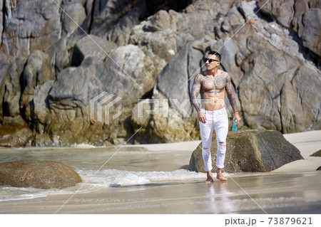 Athletic tattooed guy walking at the tropical beach Athletic tattooed guy walking at the tropical beach 73879621