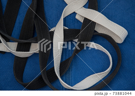 Top view, black and white belts intertwined on a blue kimono. The master and the novice, the Concept. Judo Top view, black and white belts intertwined on a blue kimono. The master and the novice, the Concept. Judo 73881044