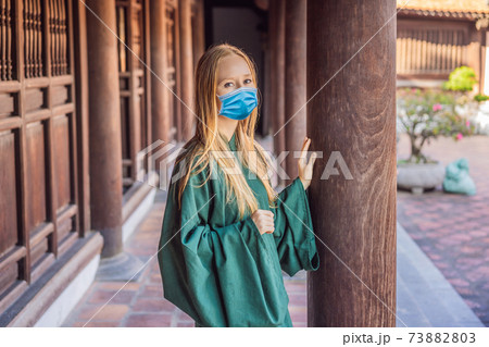 Woman tourist wearing a medical mask during COVID-19 coronavirus in national vietnamese dress in Temple of Literature in Hanoi in Southeast Asia, Vietnam. Vietnam reopens after coronavirus quarantine Woman tourist wearing a medical mask during COVID-19 coronavirus in national vietnamese dress in Temple of Literature in Hanoi in Southeast Asia, Vietnam. Vietnam reopens after coronavirus quarantine 73882803
