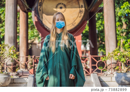 Woman tourist wearing a medical mask during COVID-19 coronavirus in national vietnamese dress in Temple of Literature in Hanoi in Southeast Asia, Vietnam. Vietnam reopens after coronavirus quarantine Woman tourist wearing a medical mask during COVID-19 coronavirus in national vietnamese dress in Temple of Literature in Hanoi in Southeast Asia, Vietnam. Vietnam reopens after coronavirus quarantine 73882899