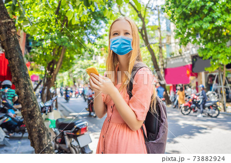 Woman using phone app for taxi ride hailing service or reading travel guide wearing a medical mask during COVID-19 coronavirus . Girl tourist searching for map directions on smartphone. Copy space Woman using phone app for taxi ride hailing service or reading travel guide wearing a medical mask during COVID-19 coronavirus . Girl tourist searching for map directions on smartphone. Copy space 73882924