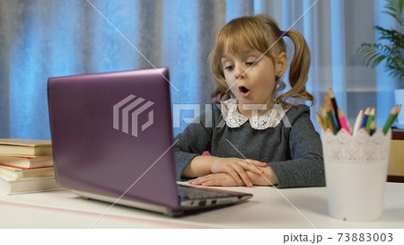 Child schoolgirl learning lessons, distance education at home sitting at table using laptop computer Child schoolgirl learning lessons, distance education at home sitting at table using laptop computer 73883003