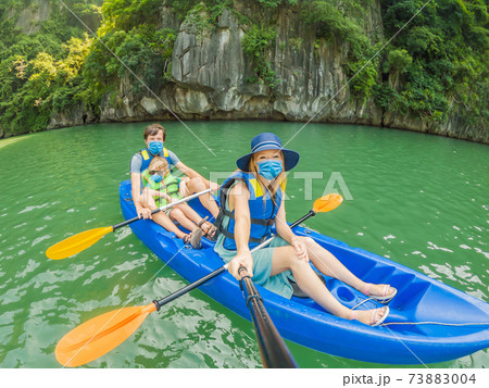 Mom, dad and son travelers wearing a medical mask during COVID-19 coronavirus rowing on a kayak in Halong Bay. Vietnam. Travel to Asia, happiness emotion, summer holiday concept. Traveling with 73883004