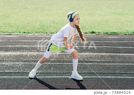 Girl jogging on a sunny summer evening, laying on treadmill, stadium, physical training, back to school. 73884314