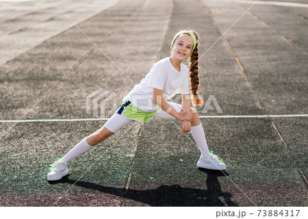 Girl jogging on a sunny summer evening, laying on treadmill, stadium, physical training, back to school. 73884317