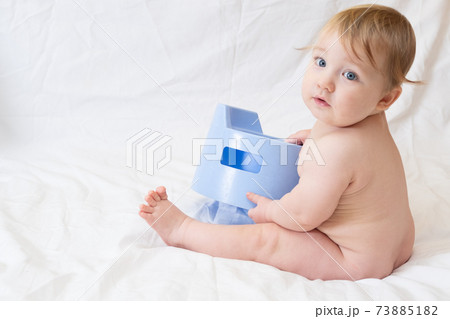 Cute blue-eyed Caucasian toddler sits near a blue nursery pot on a 73885182